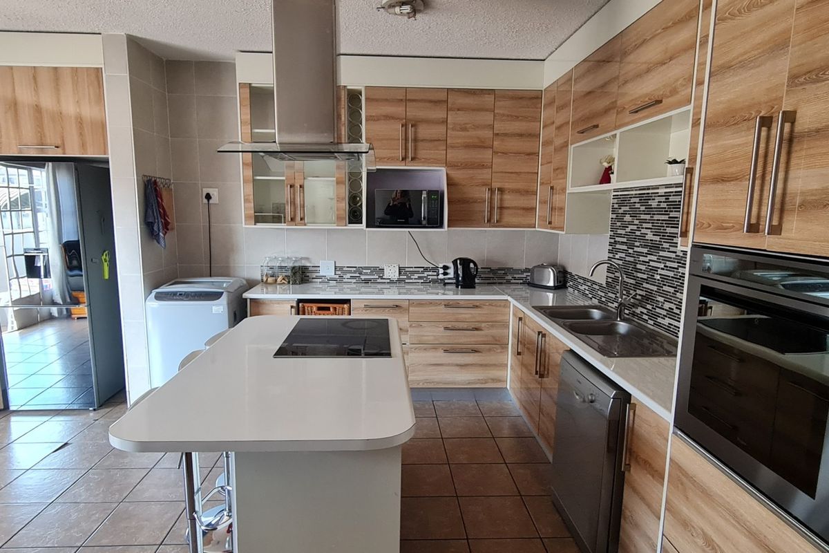 Modern kitchen featuring wood-look cabinetry, a central island with a built-in hob, stainless steel extractor fan, integrated oven, and tiled flooring.