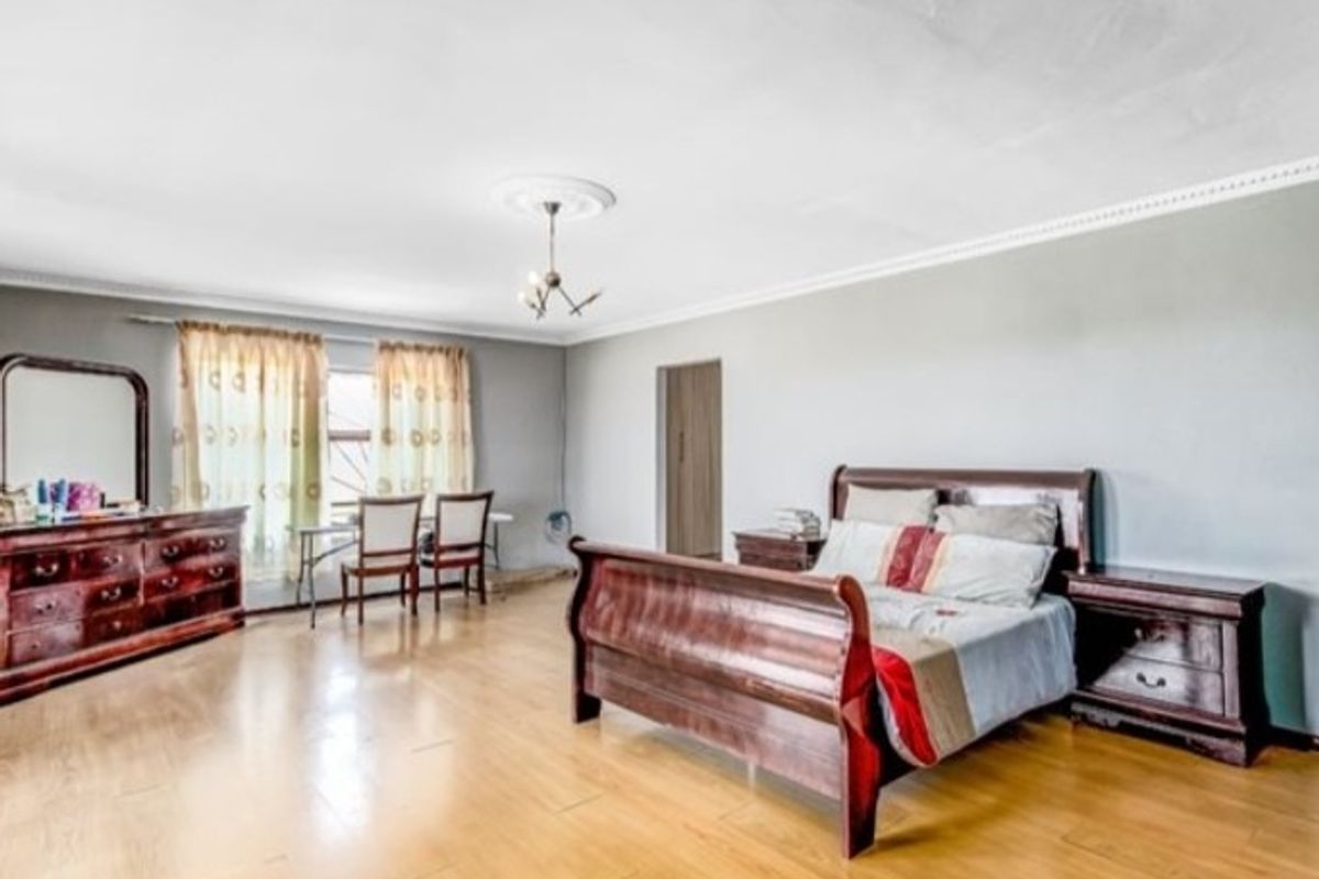 Spacious bedroom featuring light wood-look flooring, decorative ceiling rose, and neutral wall tones, offering a comfortable and functional living space.