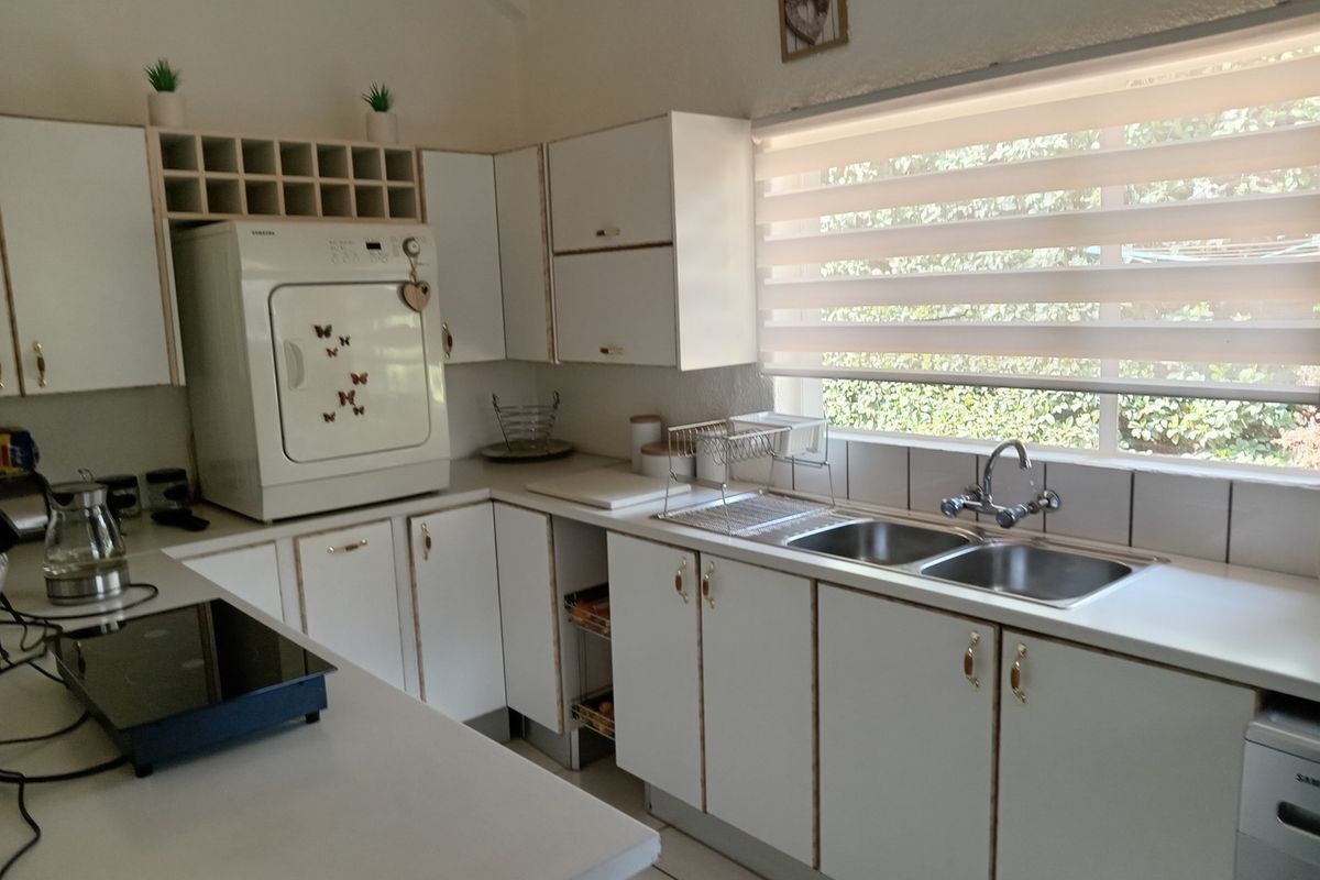 A functional kitchen featuring white cabinetry, a double stainless steel sink, tiled splashbacks, and a window with fitted blinds.