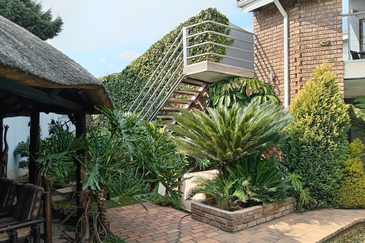 A well-maintained rear garden area featuring a brick-paved patio, a thatched gazebo, and an external metal staircase leading to an upper level.