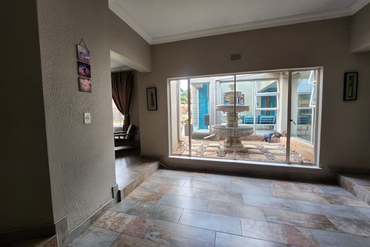 A living area featuring large windows overlooking an internal courtyard with a stone fountain, finished with tiled flooring and neutral wall tones.