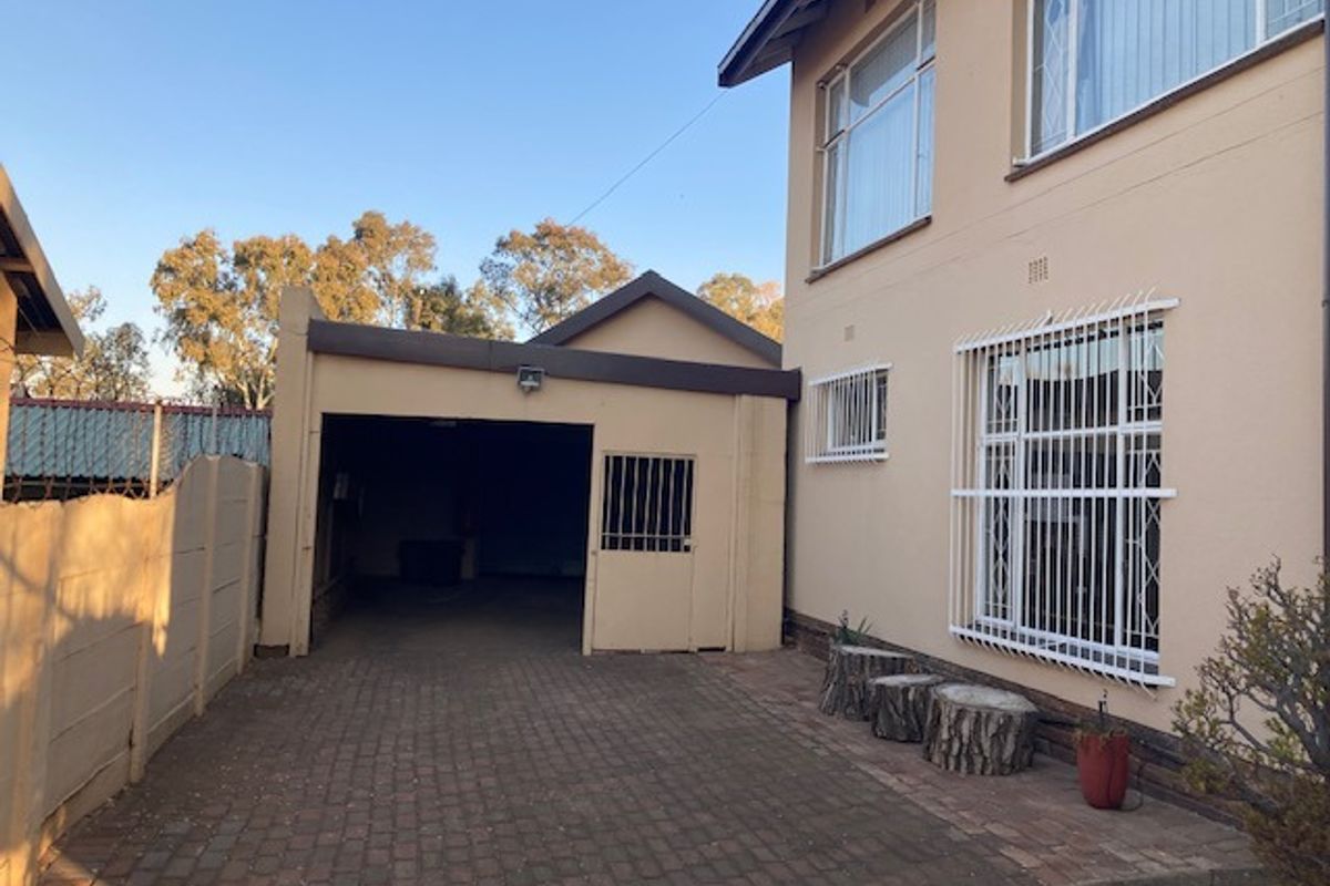 Side view of the property featuring a paved driveway leading to a single garage, with security bars installed on windows.