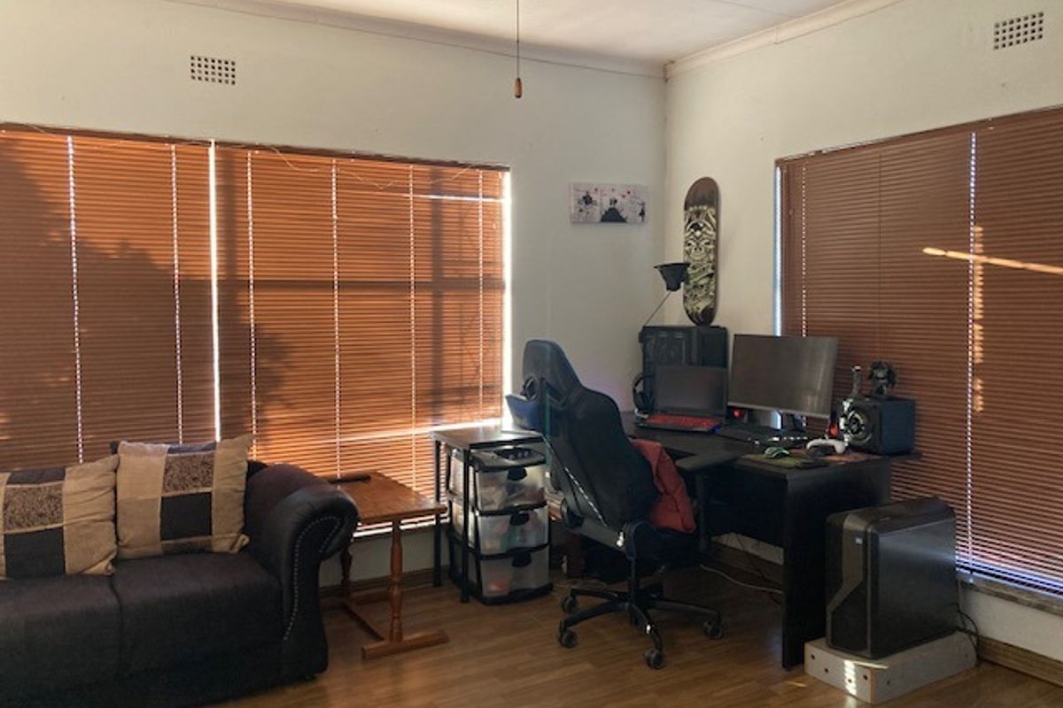A functional living area featuring wood-look laminate flooring, large windows with fitted venetian blinds, and a ceiling fan.