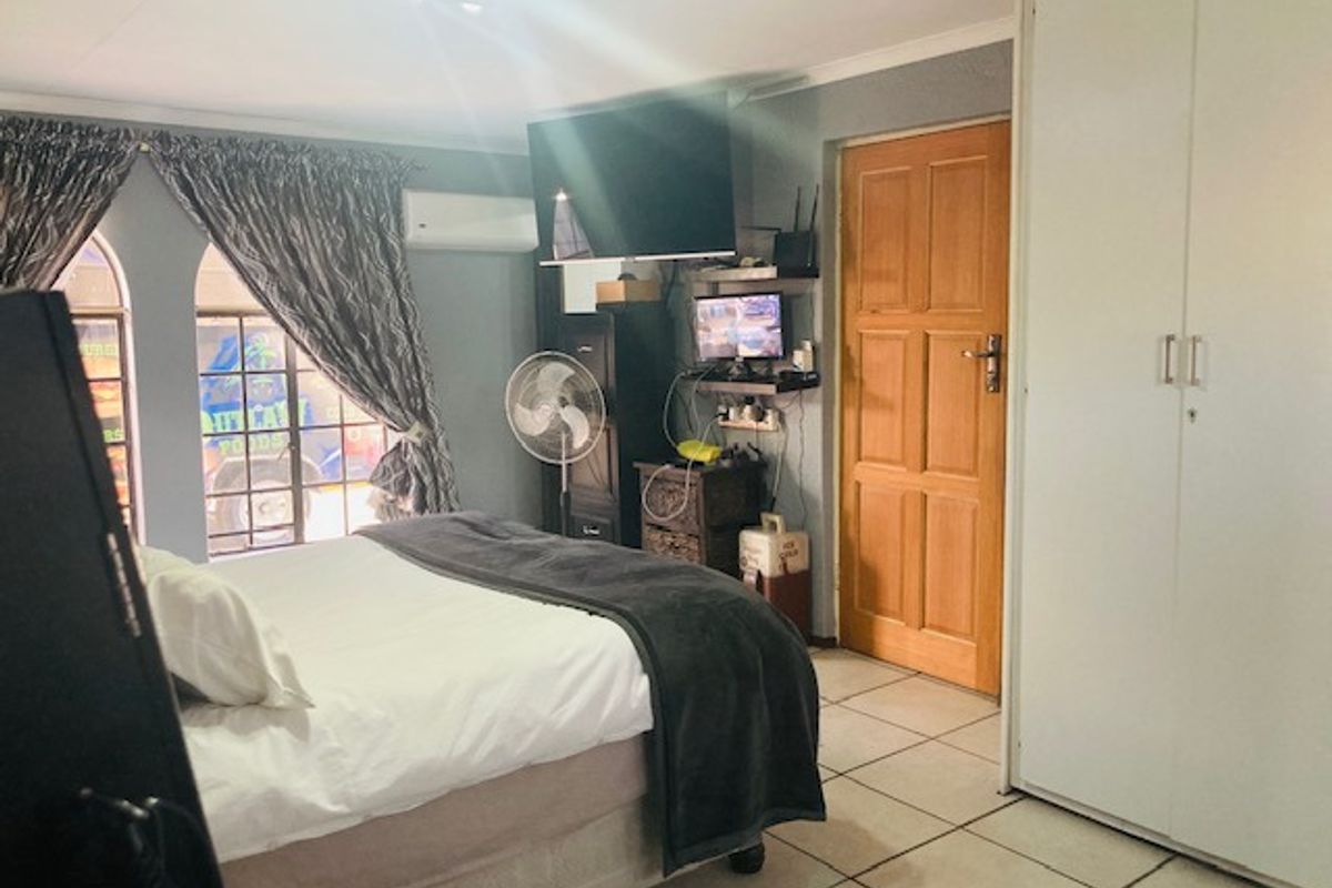 A bedroom featuring tiled flooring, built-in cupboards, and a wall-mounted air conditioning unit.