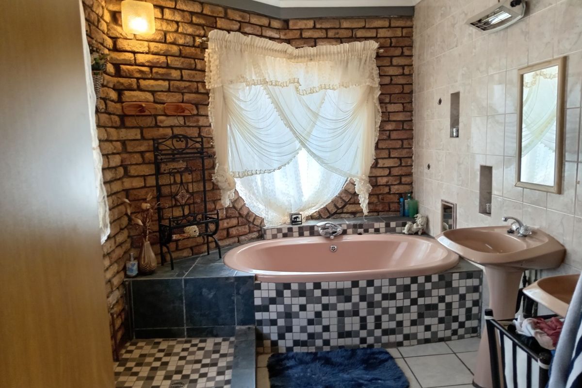 A dated bathroom featuring a built-in bathtub, pedestal basin, and exposed brick wall detailing with tiled flooring.