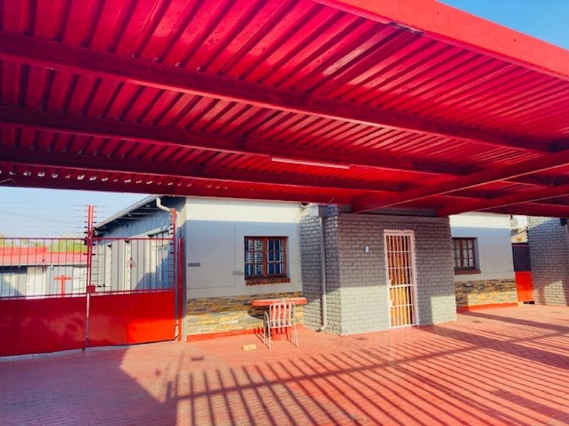 Front exterior view featuring a large red corrugated metal carport, brick and stone facade, and secure gated entrance.