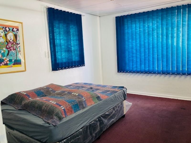 A functional bedroom featuring carpeted flooring and blue vertical window blinds, providing a simple and neutral space.