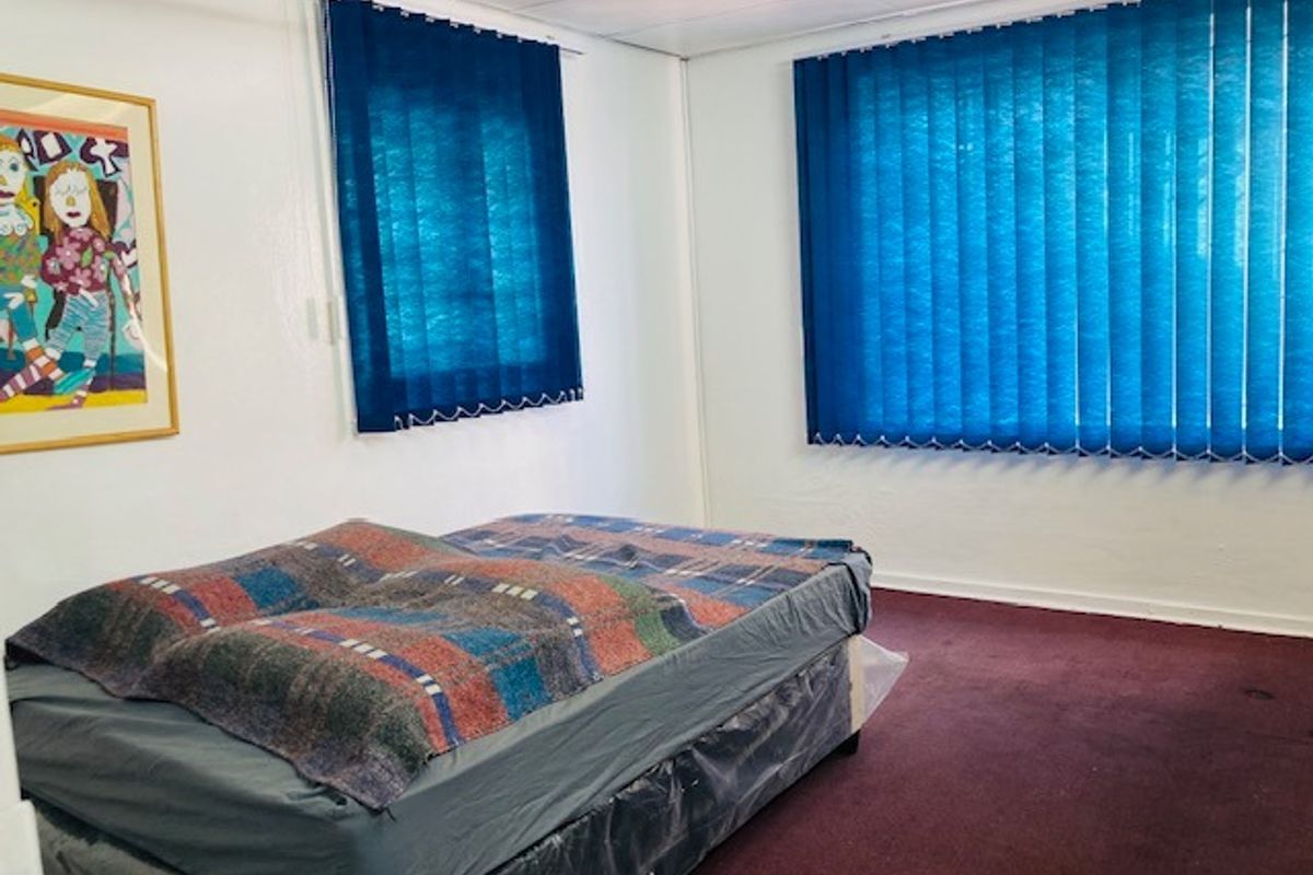 A functional bedroom featuring carpeted flooring and blue vertical window blinds, providing a simple and neutral space.