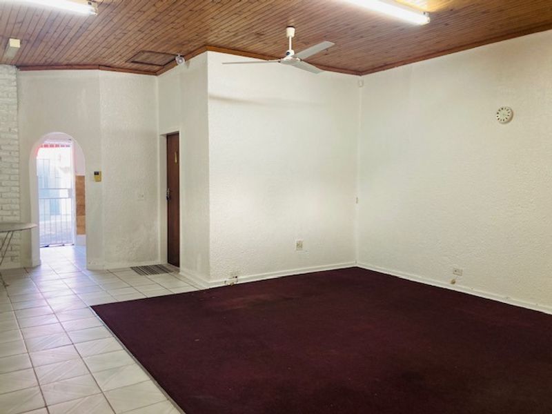 Spacious living area featuring a timber-clad ceiling, ceiling fan, and a combination of tiled and carpeted flooring with an arched entryway.