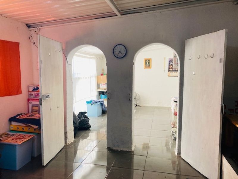 A functional hallway area featuring arched doorways, tiled flooring, and a corrugated metal ceiling, providing access to adjacent rooms.