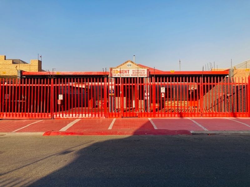 Front exterior view of the property featuring a prominent red steel security fence, paved driveway, and street-facing signage.