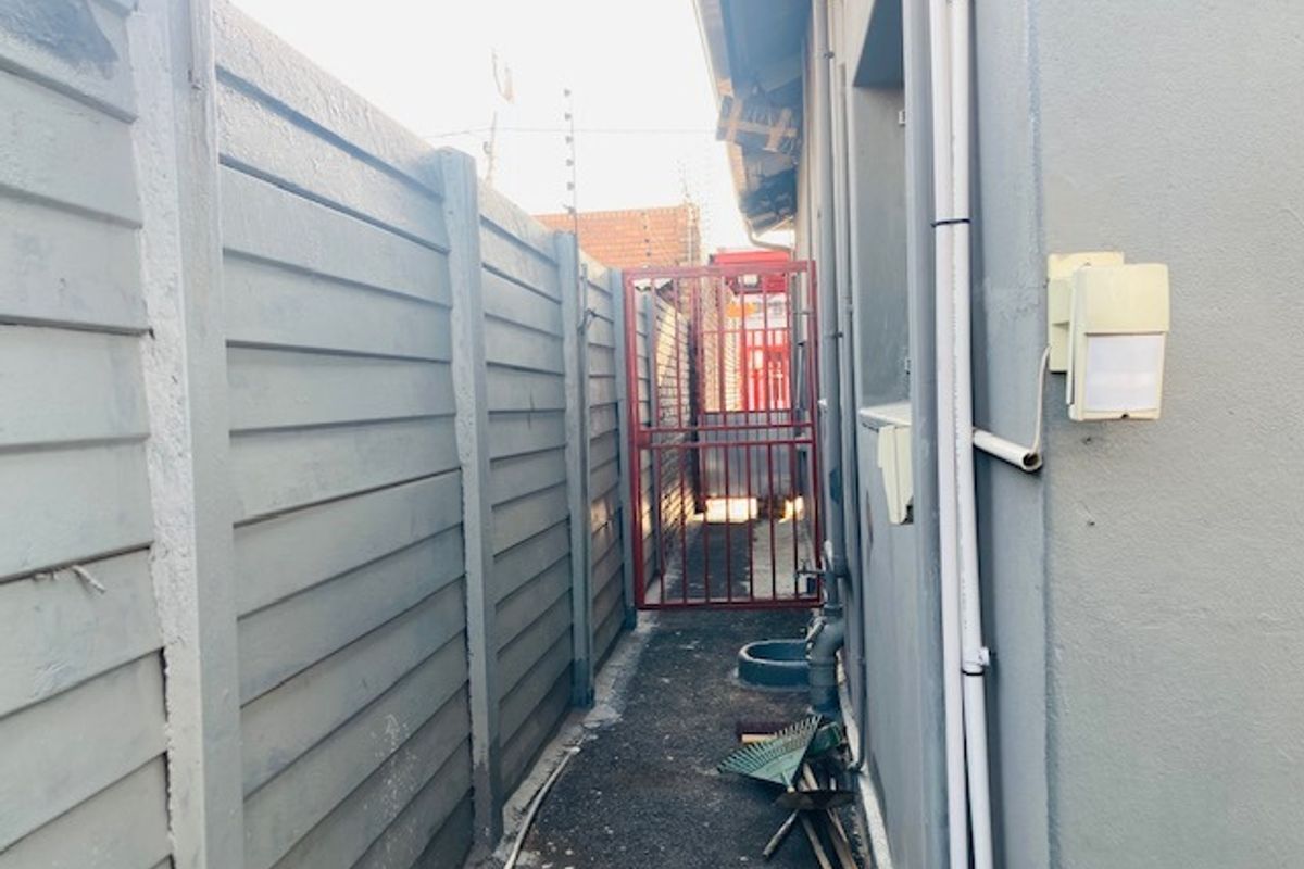 A narrow side passage featuring a precast concrete boundary wall, electric fencing, and a secure metal gate providing access to the rear of the property.