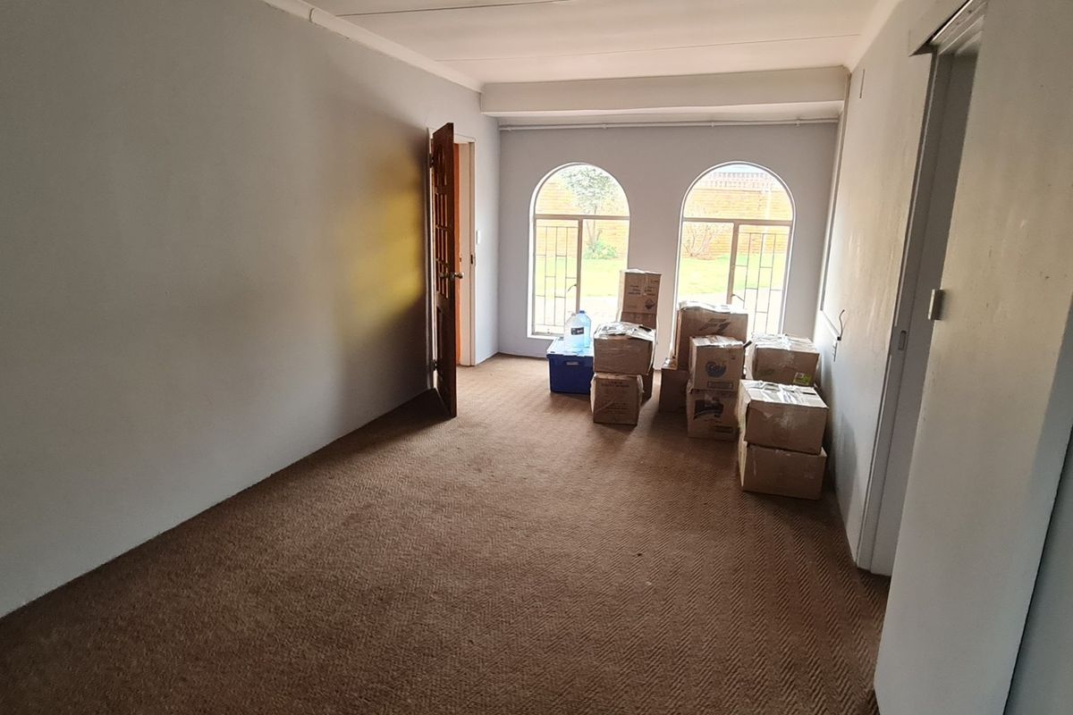 A vacant living room featuring brown carpeting, arched windows with security bars, and neutral wall finishes, offering a blank canvas for potential updates.