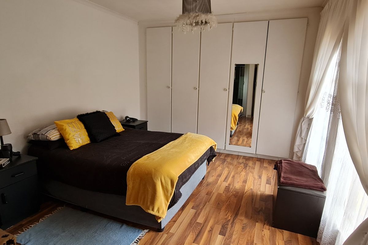 A well-lit bedroom featuring built-in floor-to-ceiling wardrobes with a central mirror and durable wood-look flooring.