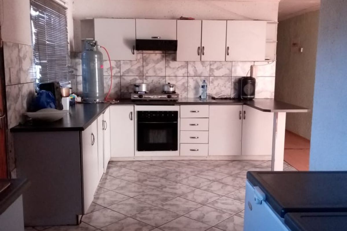 A functional kitchen featuring white cabinetry, a built-in oven, hob, extractor fan, and tiled flooring with a breakfast bar extension.