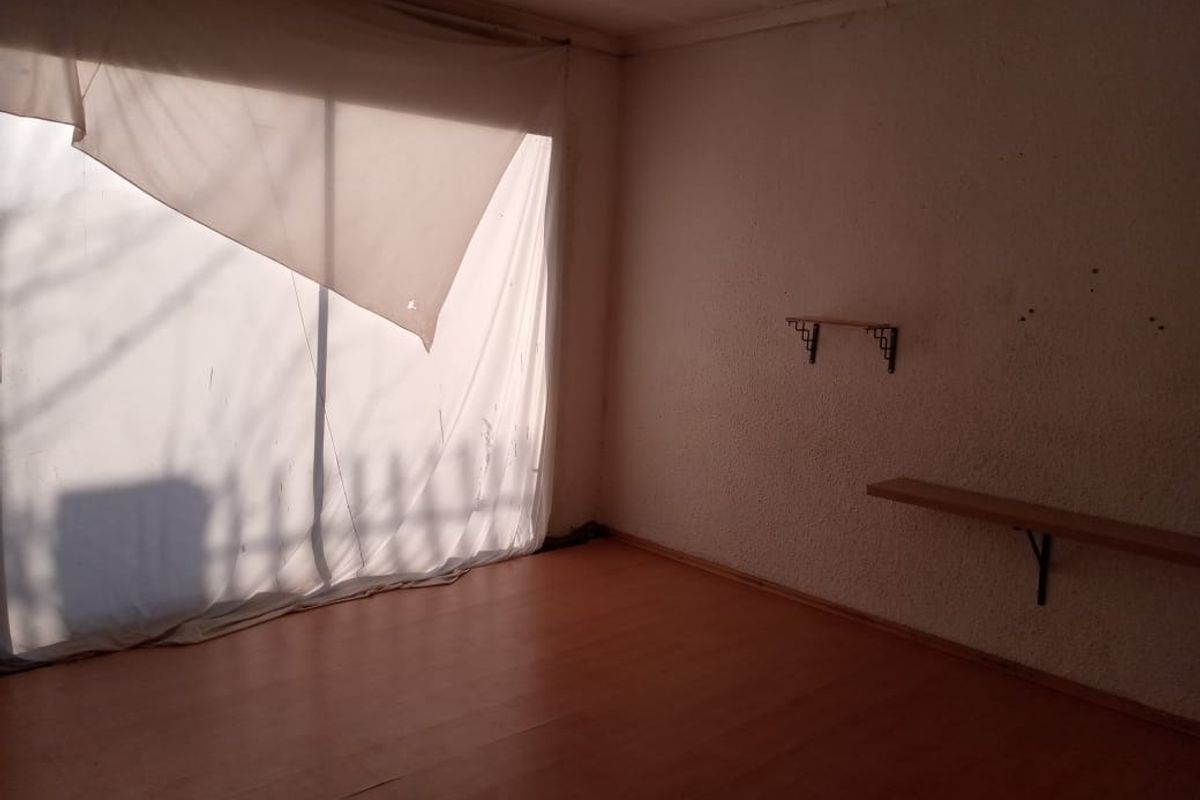 An empty bedroom featuring laminate flooring, textured walls, and a large window covered by a makeshift fabric screen.