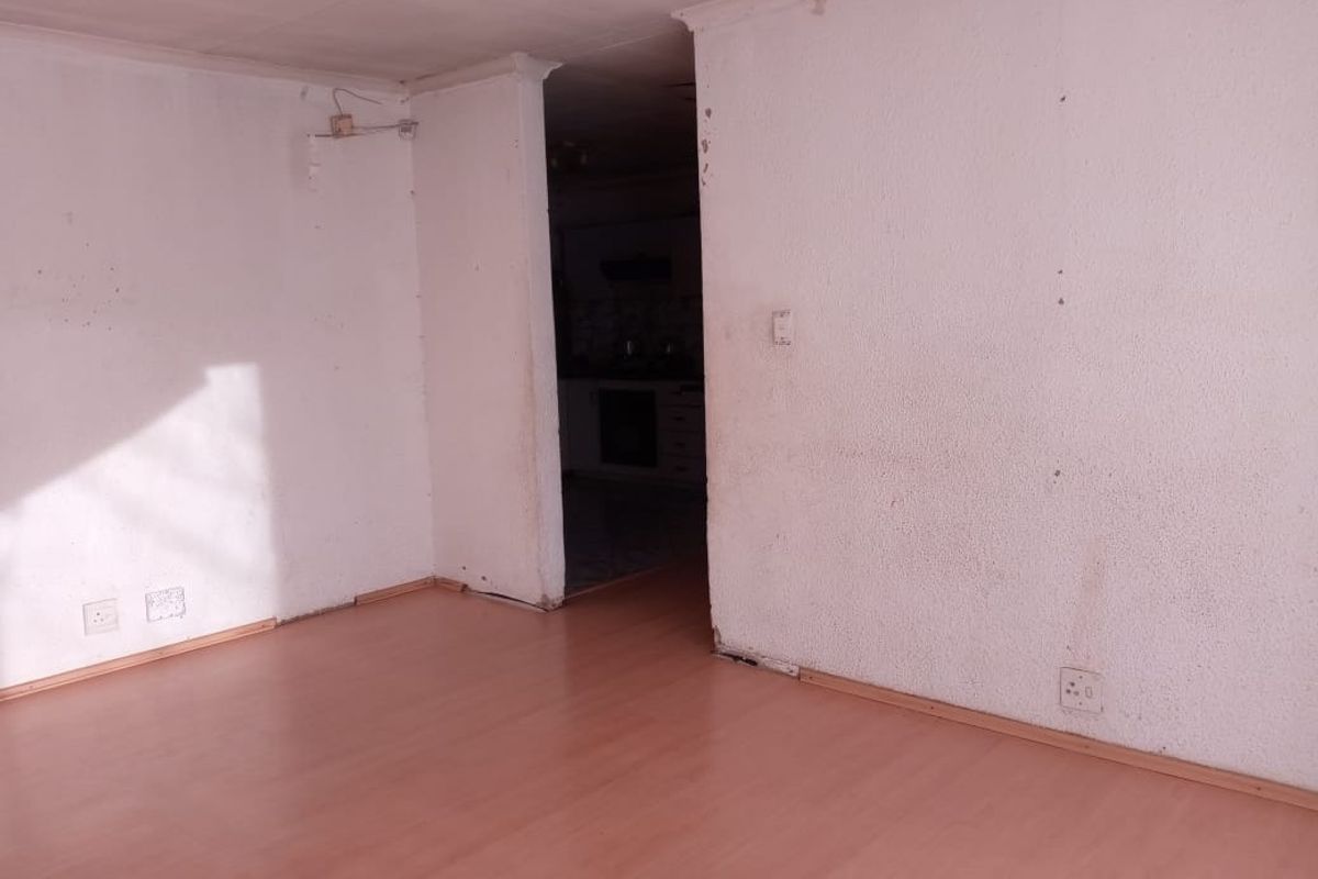 An empty living area featuring laminate flooring and direct access to an adjacent kitchen space, requiring cosmetic updates to the walls and finishes.
