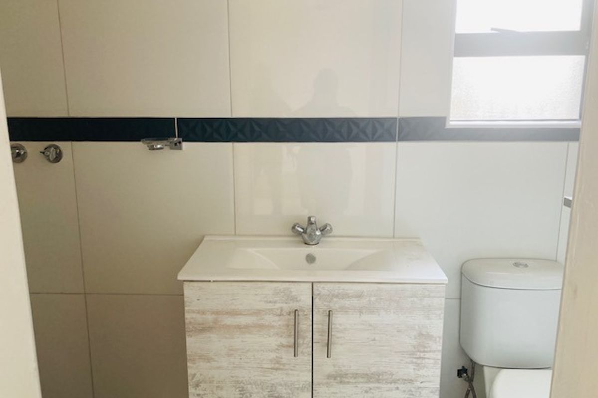 A clean bathroom featuring a modern vanity with integrated basin, a standard toilet, and tiled walls with a decorative accent border.