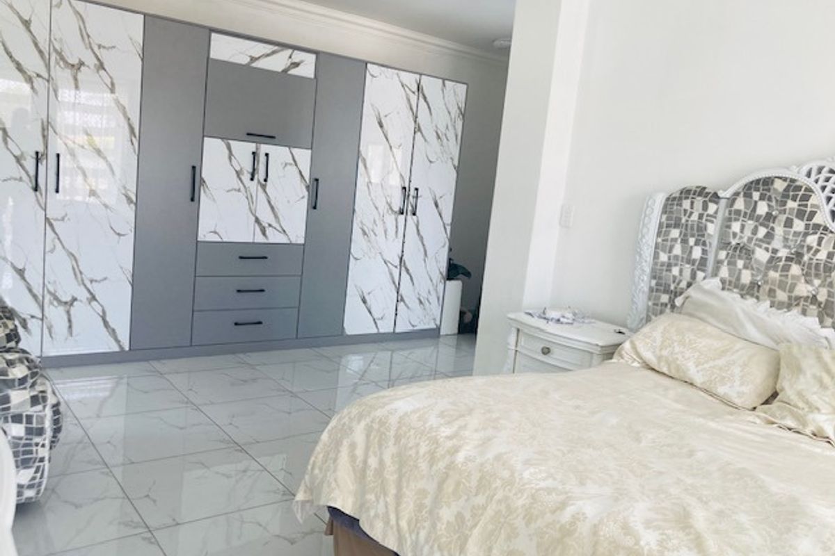 Spacious bedroom featuring large built-in wardrobes with a modern marble-effect and grey finish, complemented by polished floor tiles.