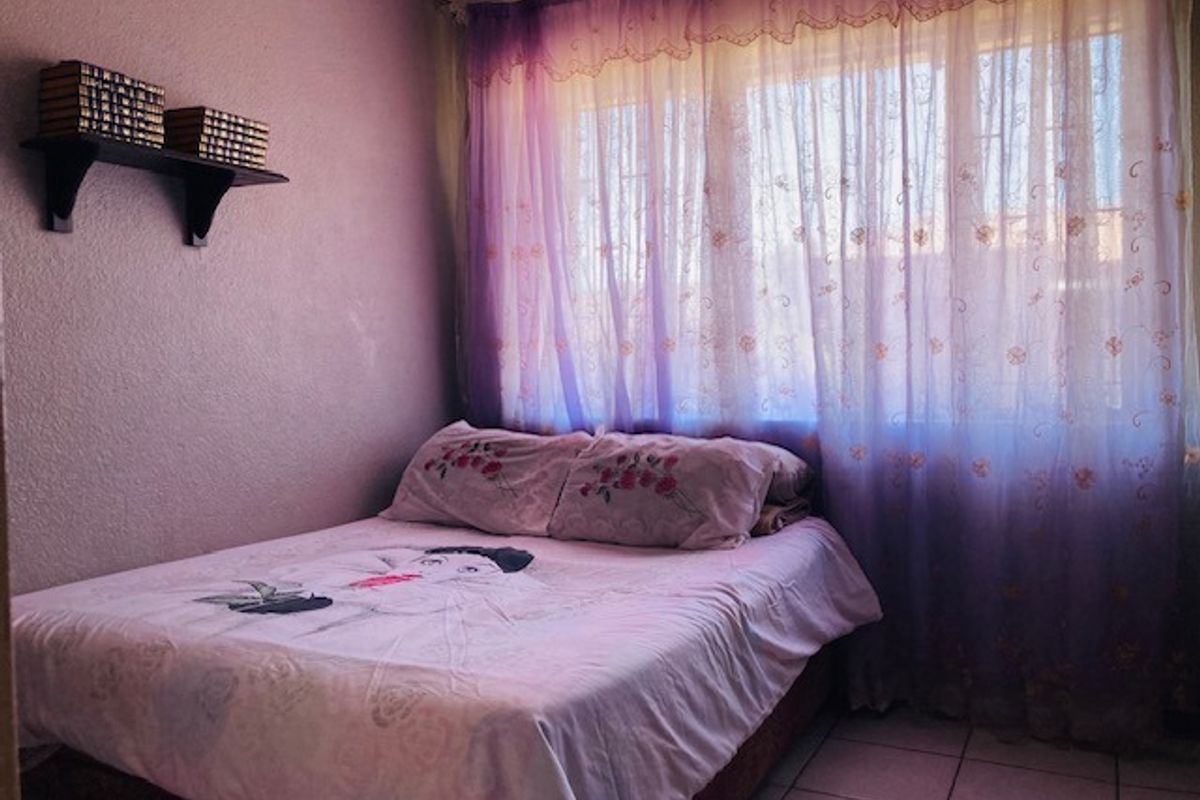 A bedroom featuring tiled flooring and a large window with sheer curtains, providing natural light to the space.