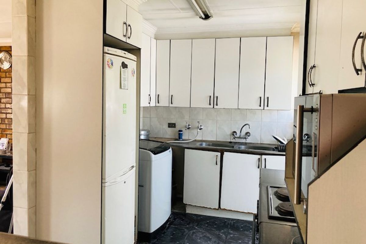 A functional kitchen featuring white cabinetry, a double sink, and tiled splashbacks, providing a practical workspace with integrated appliance storage.