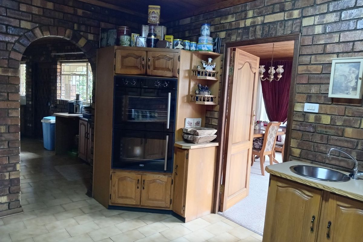 A dated kitchen featuring exposed brick walls, timber cabinetry, and a built-in double oven, with an arched entryway leading to an adjacent space.