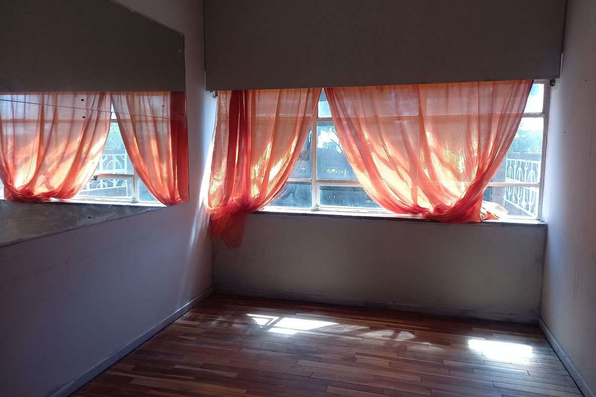 A bright, empty bedroom featuring polished timber flooring, a large wall-mounted mirror, and expansive windows with natural light.