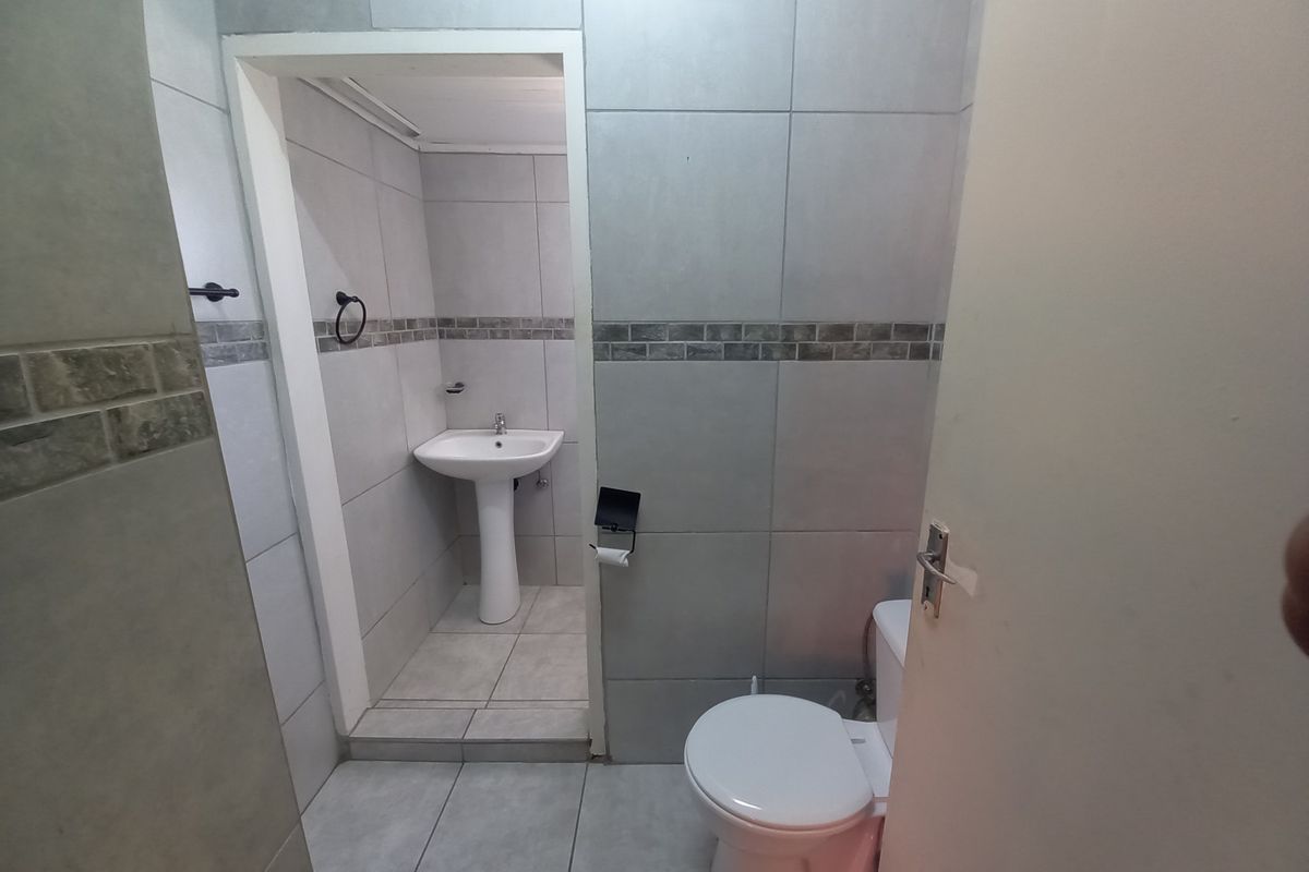 A functional bathroom featuring a pedestal basin and a standard toilet, finished with neutral wall and floor tiling.