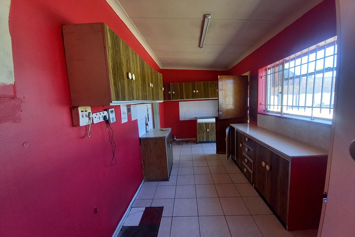 A dated kitchen featuring wood-finish cabinetry, tiled flooring, and bright red walls, offering a functional layout ready for modernization.