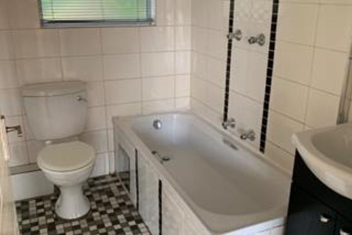 A functional bathroom featuring a standard bathtub, toilet, and vanity basin with tiled walls and flooring.