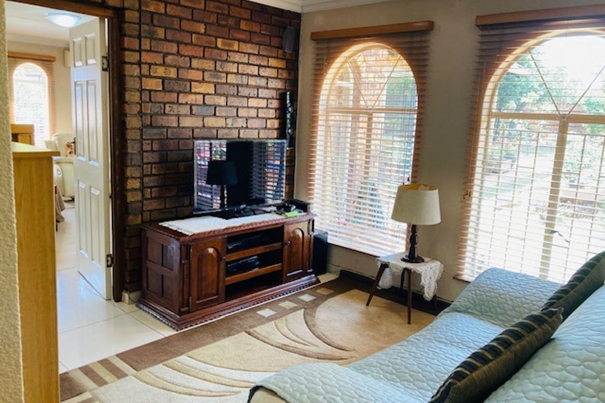 A cozy living room featuring a distinctive exposed brick feature wall, arched windows with fitted blinds, and tiled flooring.