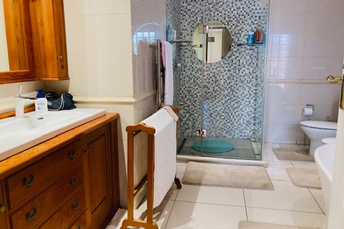 A functional bathroom featuring a wooden vanity, a glass-enclosed shower with mosaic tile accents, and a separate toilet area.