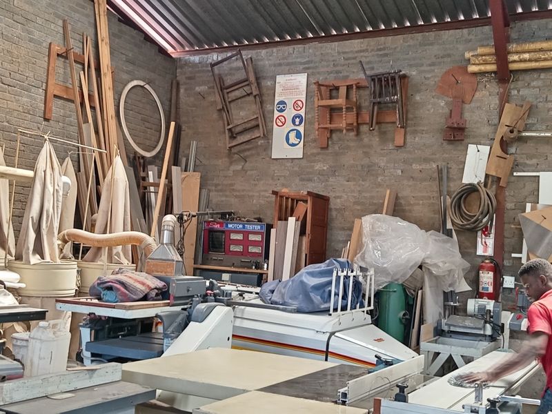 Industrial workshop space featuring exposed brick walls, corrugated metal roofing, and integrated dust extraction systems for heavy machinery.