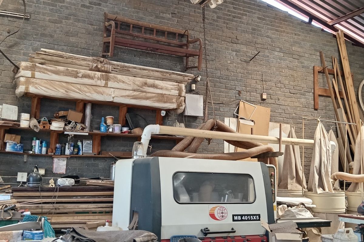 Industrial workshop space featuring exposed brick walls, high-pitched metal roofing, and integrated dust extraction infrastructure for heavy-duty manufacturing or carpentry use.