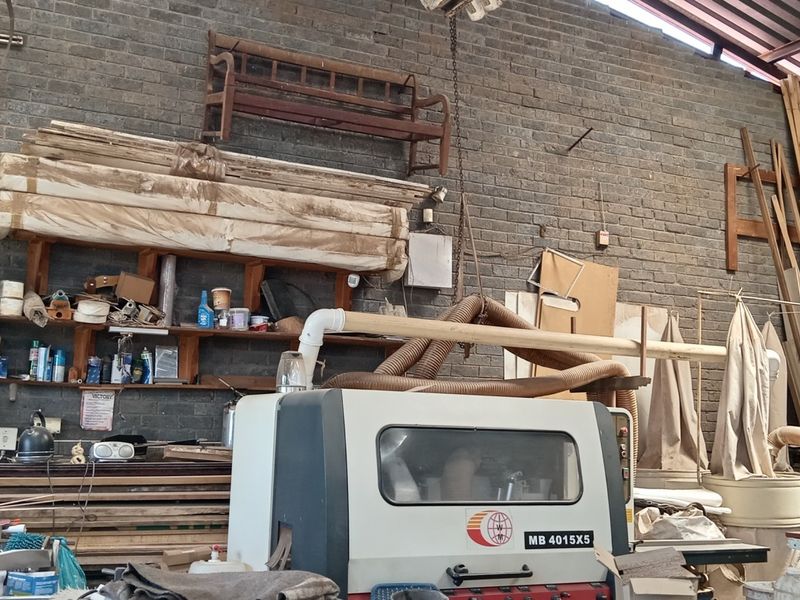 Industrial workshop space featuring exposed brick walls, high-pitched metal roofing, and integrated dust extraction infrastructure for heavy-duty manufacturing or carpentry use.