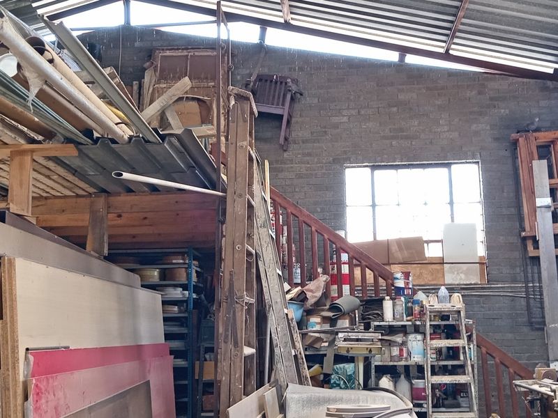 Industrial utility space featuring exposed brick walls, a corrugated metal roof, and a mezzanine level accessed by a timber staircase.