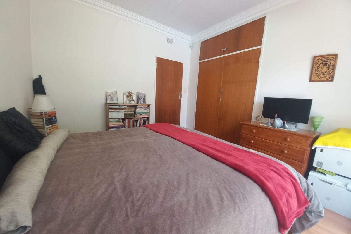 A functional bedroom featuring built-in wooden wardrobes, laminate flooring, and classic ceiling cornicing, offering a neutral base for potential updates.