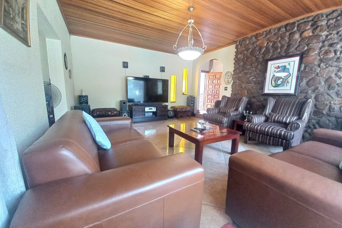 Spacious living room featuring a distinctive stone feature wall, warm timber-clad ceiling, and neutral tiled flooring, creating a rustic and inviting atmosphere.