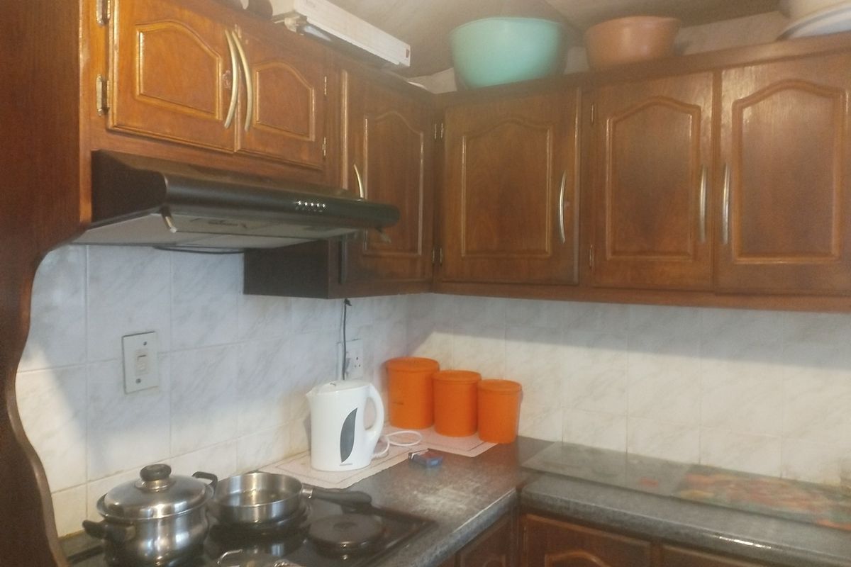 A compact kitchen featuring traditional wooden cabinetry, a built-in extractor fan, and a tiled backsplash with a functional cooktop.
