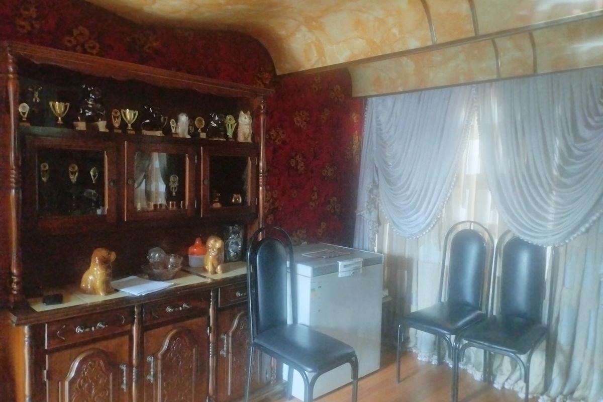 A dated living area featuring traditional wall coverings, a built-in wooden display cabinet, and a curved ceiling design.