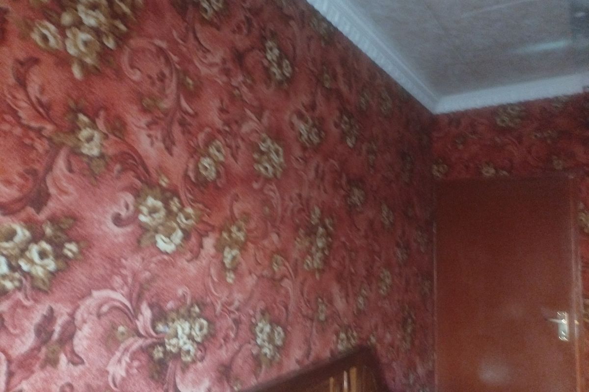 A bedroom interior featuring traditional floral patterned wallpaper and decorative ceiling cornicing.