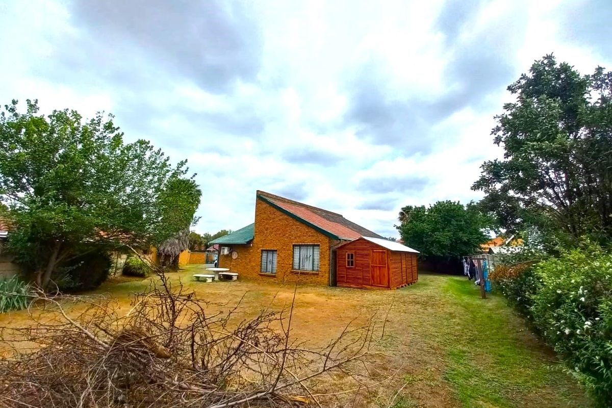 Rear view of the property featuring a brick facade, pitched roof, and a detached timber shed set within a spacious garden area.
