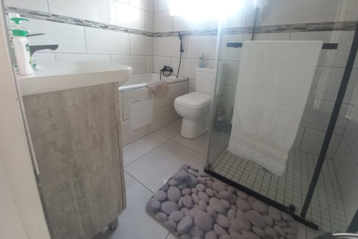 A modern bathroom featuring a vanity basin, a bathtub, a toilet, and a glass-enclosed shower with neutral wall and floor tiling.