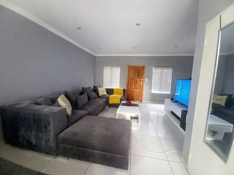 A spacious living room featuring neutral grey walls, polished tiled flooring, recessed downlights, and natural light through venetian blinds.