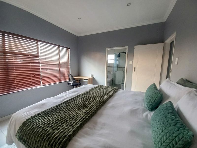 A well-maintained bedroom featuring neutral grey walls, recessed downlighting, venetian blinds, and direct access to an en-suite bathroom.