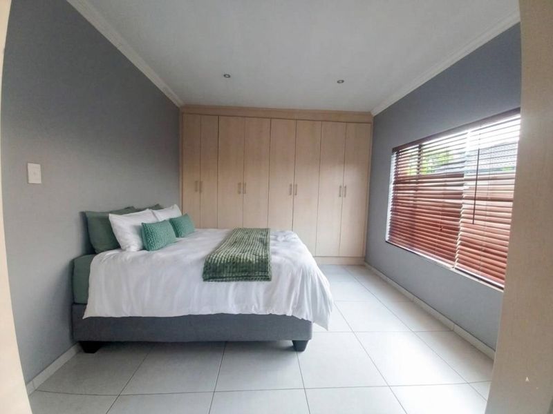 A well-maintained bedroom featuring neutral grey walls, light wood built-in cupboards, tiled flooring, and venetian blinds.