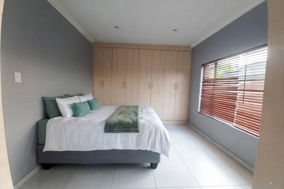 A well-maintained bedroom featuring neutral grey walls, light wood built-in cupboards, tiled flooring, and venetian blinds.