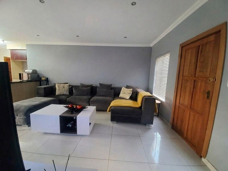 Open plan living area featuring tiled flooring, recessed downlights, and a wooden door, with a partial view of the adjacent kitchen area.