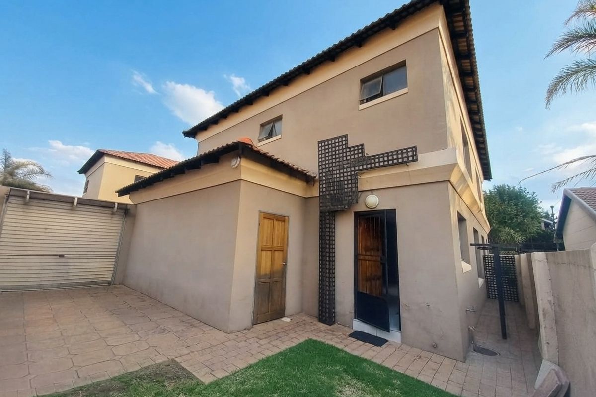 Rear view of a two-story house featuring a paved patio area, a garage, and a small garden space.