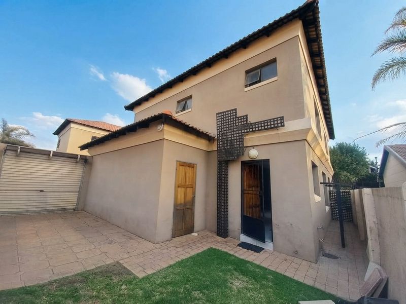 Rear view of a two-story house featuring a paved patio area, a garage, and a small garden space.